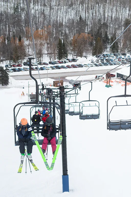 Skiers riding a ski lift up a snowy hill